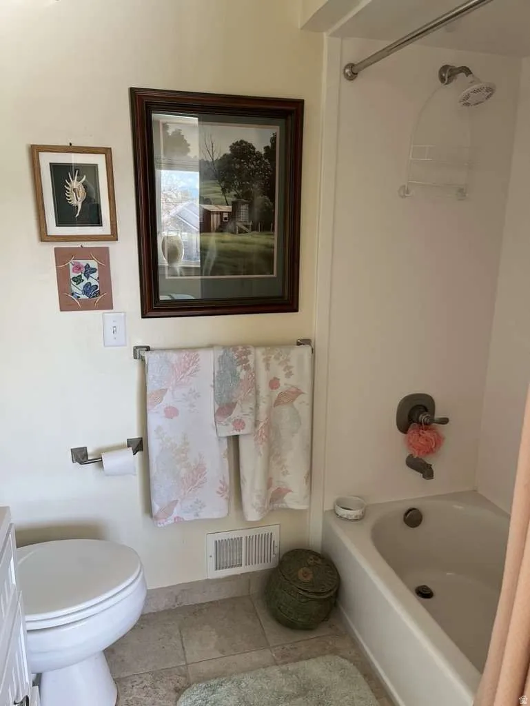 Bathroom featuring a tiled floor, white tub/shower combination with a brushed nickel showerhead, and a white toilet
