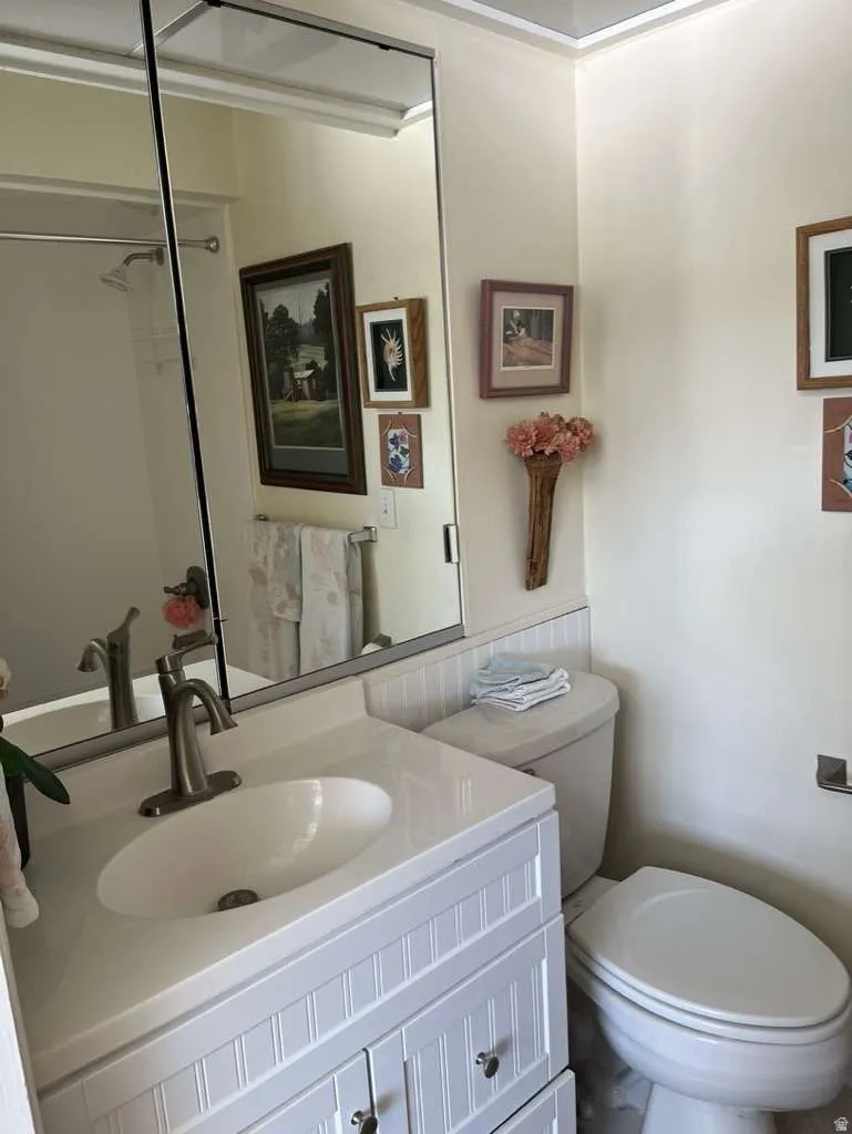 Bathroom featuring a white beadboard vanity with an integrated sink and brushed nickel faucet, a frameless wall-mounted mirror, and white wainscoting