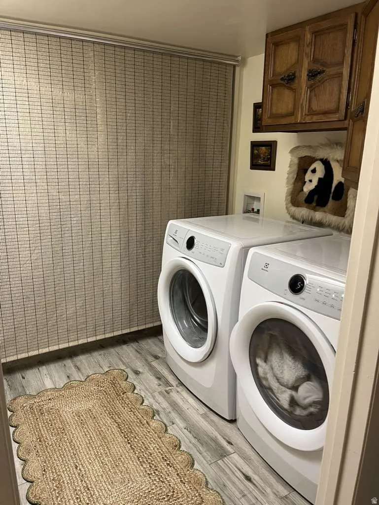 Laundry area featuring wood-finish flooring, overhead cabinetry, and horizontal window blinds