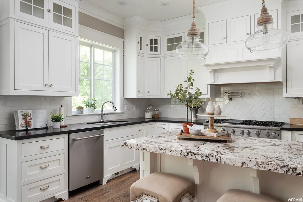 Modern kitchen featuring white cabinetry, a large kitchen island with a stone-finish countertop, stainless steel appliances, a herringbone tile backsplash, and wood-finish flooring