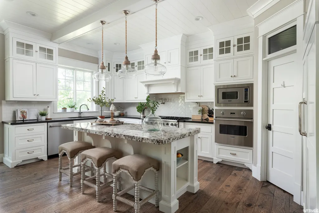 Kitchen featuring white shaker-style cabinetry, wood-finish flooring, a central island with a stone countertop, stainless steel appliances, and glass pendant lighting
