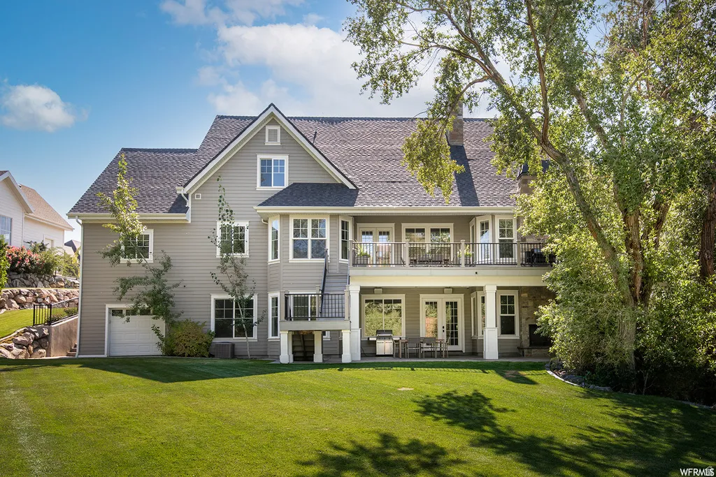 Expansive rear exterior featuring a multi-level design, a generous lawn, a covered patio, an upper-level balcony, and a lower-level garage access