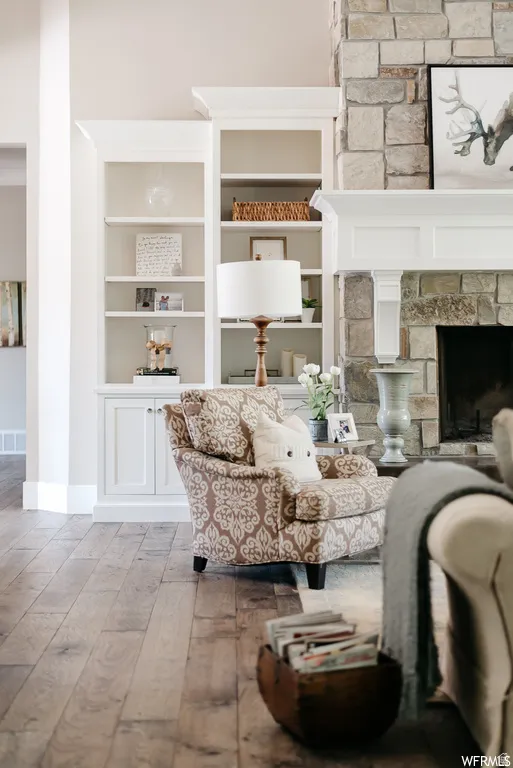 Built-in shelving units flank a stone-clad fireplace with a white mantel, complemented by wide plank wood-finish flooring