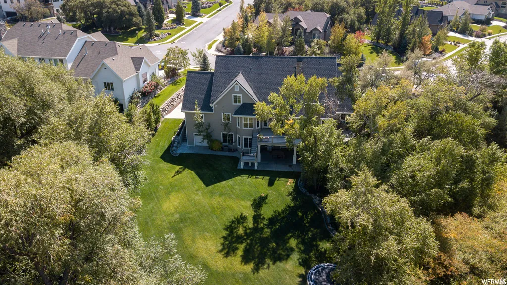 Spacious backyard with a manicured lawn, mature trees, and a multi-level dwelling featuring a covered patio and upper-level deck