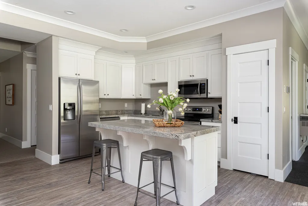 Kitchen featuring white cabinetry, stainless steel appliances, a center island with seating, stone countertops, and wood-finish flooring
