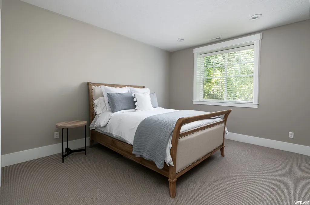 Neutral-toned bedroom featuring recessed lighting, a large window with white trim, and plush carpeting