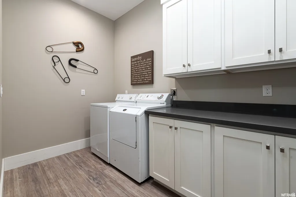 Dedicated utility room featuring wood-finish flooring, white cabinetry with dark hardware, and dark countertops
