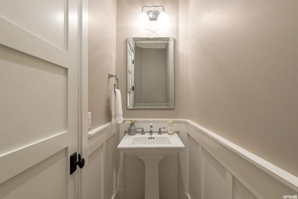 Pedestal sink with chrome faucet, complemented by a rectangular framed mirror and wall-mounted vanity lighting