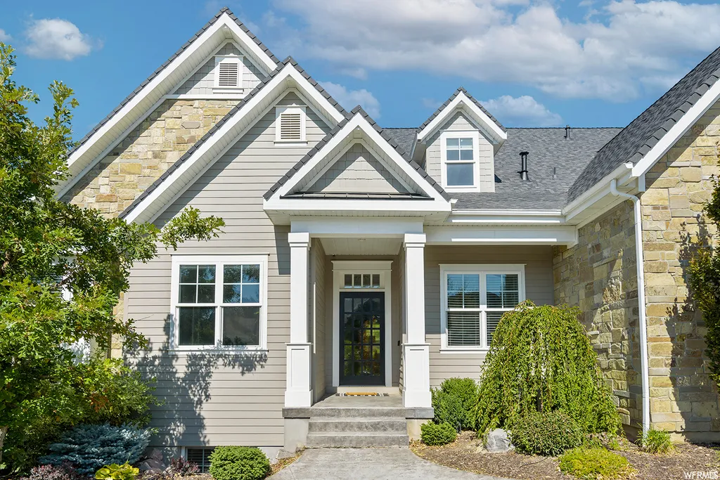 Front exterior featuring stone and siding finishes, multiple gables, an inviting covered entryway, and mature landscaping
