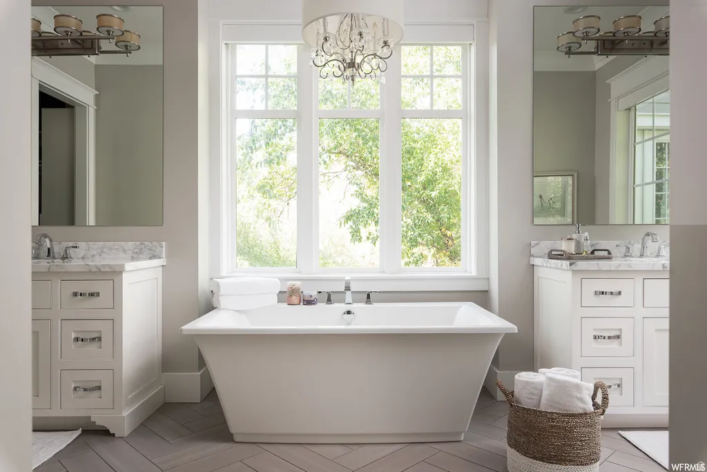 Freestanding soaking tub with a chandelier overhead and herringbone-patterned wood-finish flooring