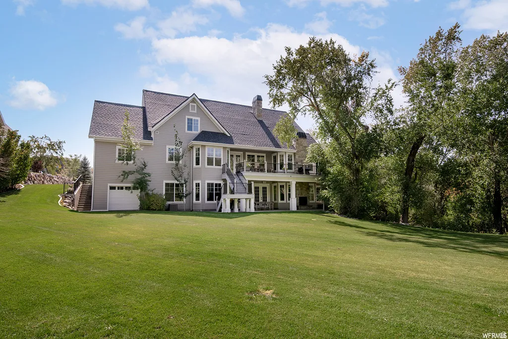 Expansive green lawn with a multi-level gray siding residence featuring a walk-out lower level, multiple windows, and exterior stairs