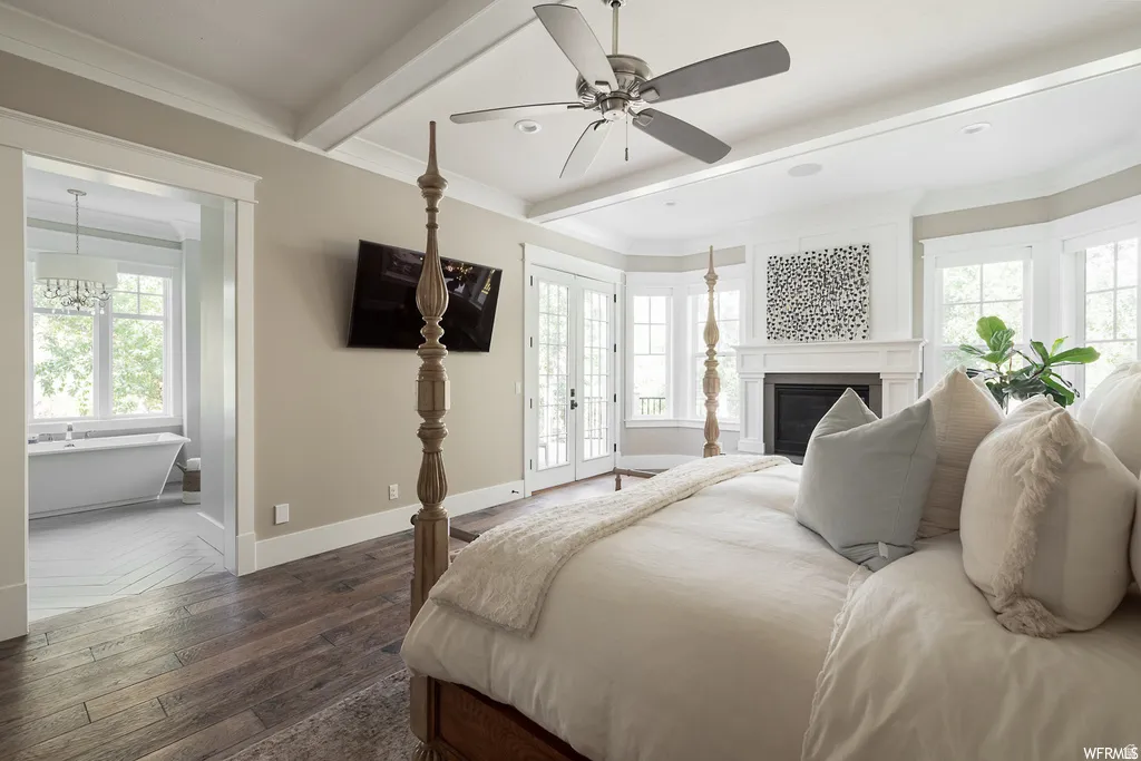 Spacious bedroom featuring wood-finish flooring, a fireplace with a white mantel, and extensive windowing