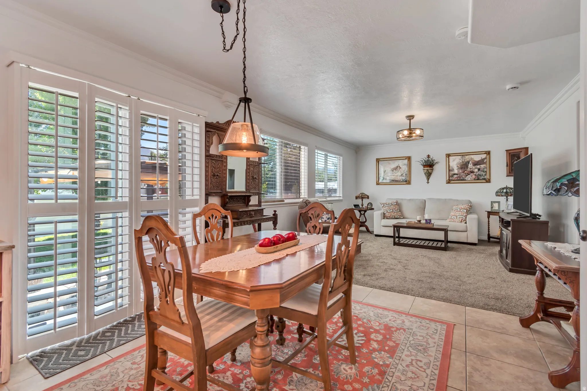 Dining area featuring ceramic tile flooring, a dark bronze pendant light fixture, and white plantation shutters on the sliding glass door