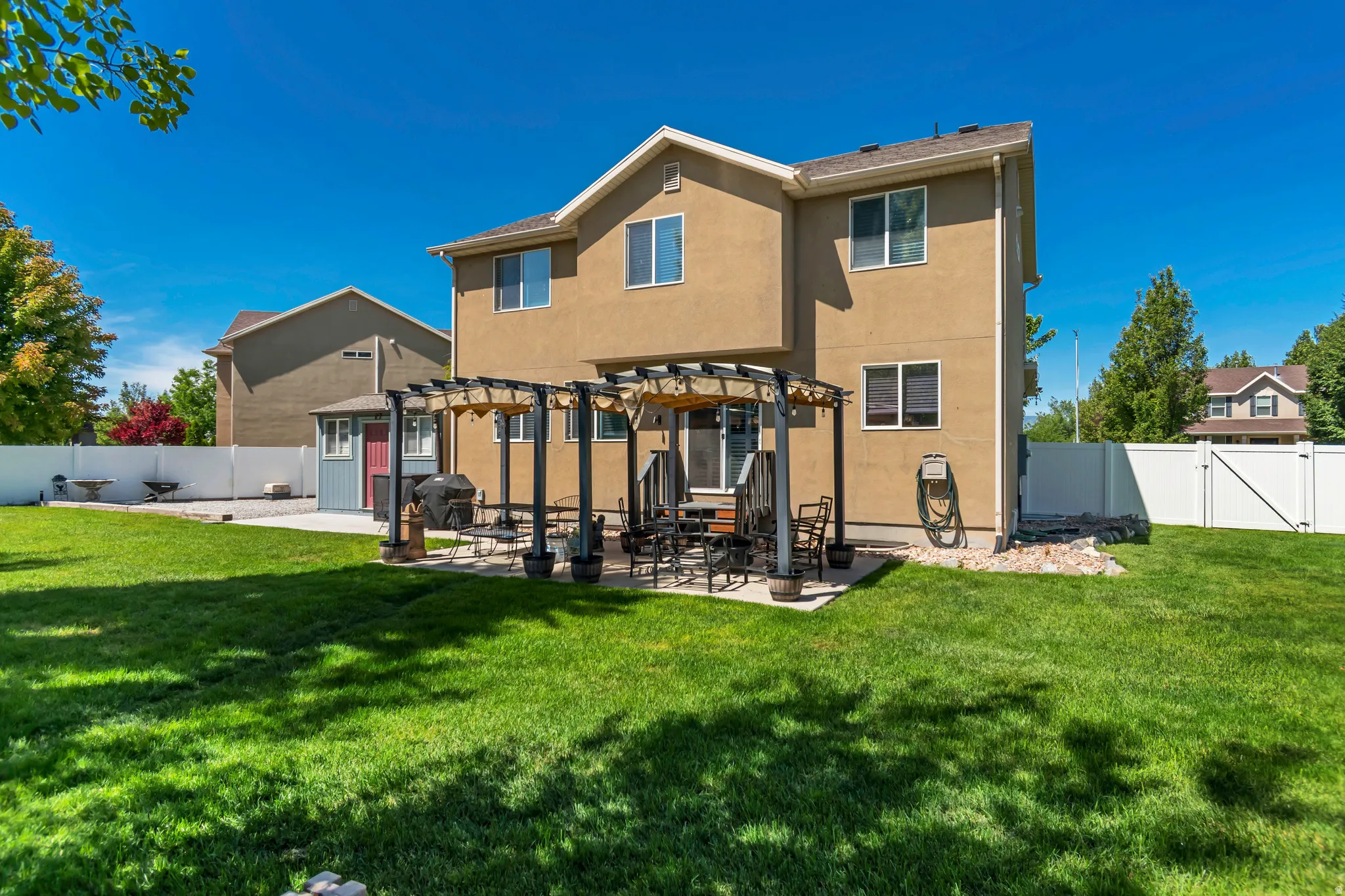 Spacious backyard featuring a large green lawn, a concrete patio with an attached pergola, and a storage shed