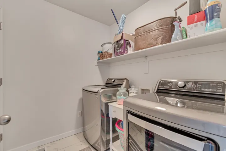 Dedicated laundry area featuring modern appliances, wall-mounted shelving, and tile flooring