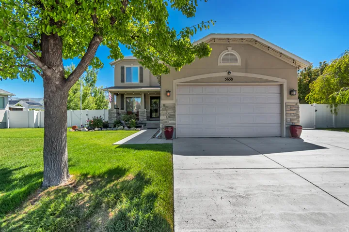 Two-story stucco and stone-accented residence featuring a two-car garage, established front yard with mature trees, and a concrete driveway