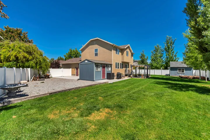 Spacious backyard featuring a manicured lawn, gravel area, and two storage sheds