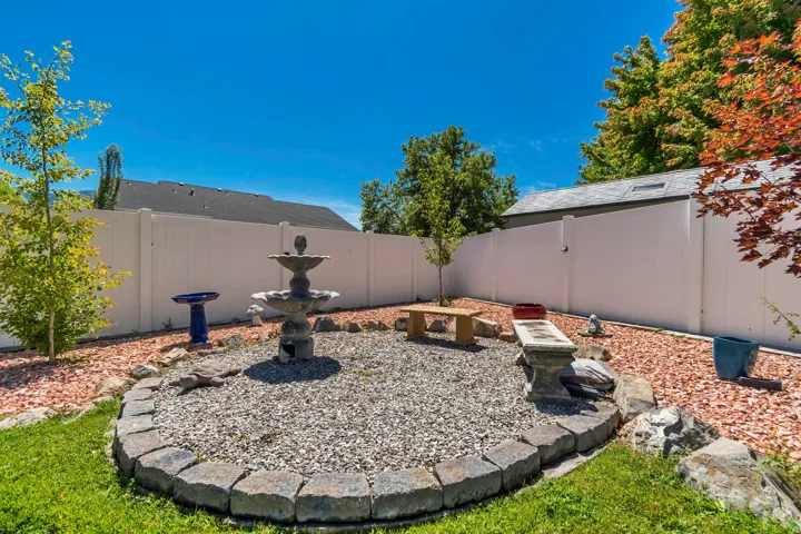 Fenced backyard featuring a tiered fountain, stone-edged gravel patio, red rock landscaping, and a manicured lawn