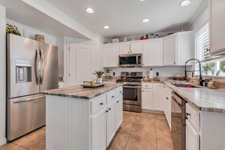 Bright kitchen featuring white cabinetry, stainless steel appliances, a center island with beadboard paneling, stone countertops, and recessed lighting