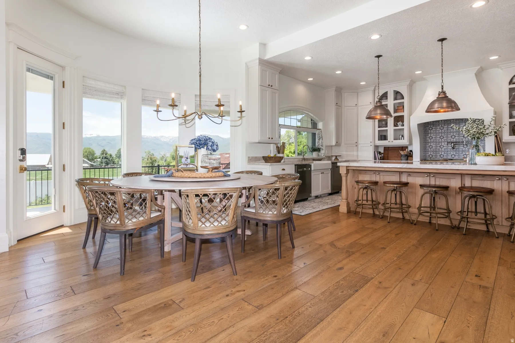 Open-concept dining area and kitchen featuring wood-finish flooring, a curved wall with multiple windows, a decorative chandelier, white cabinetry, and a kitchen island with pendant lighting