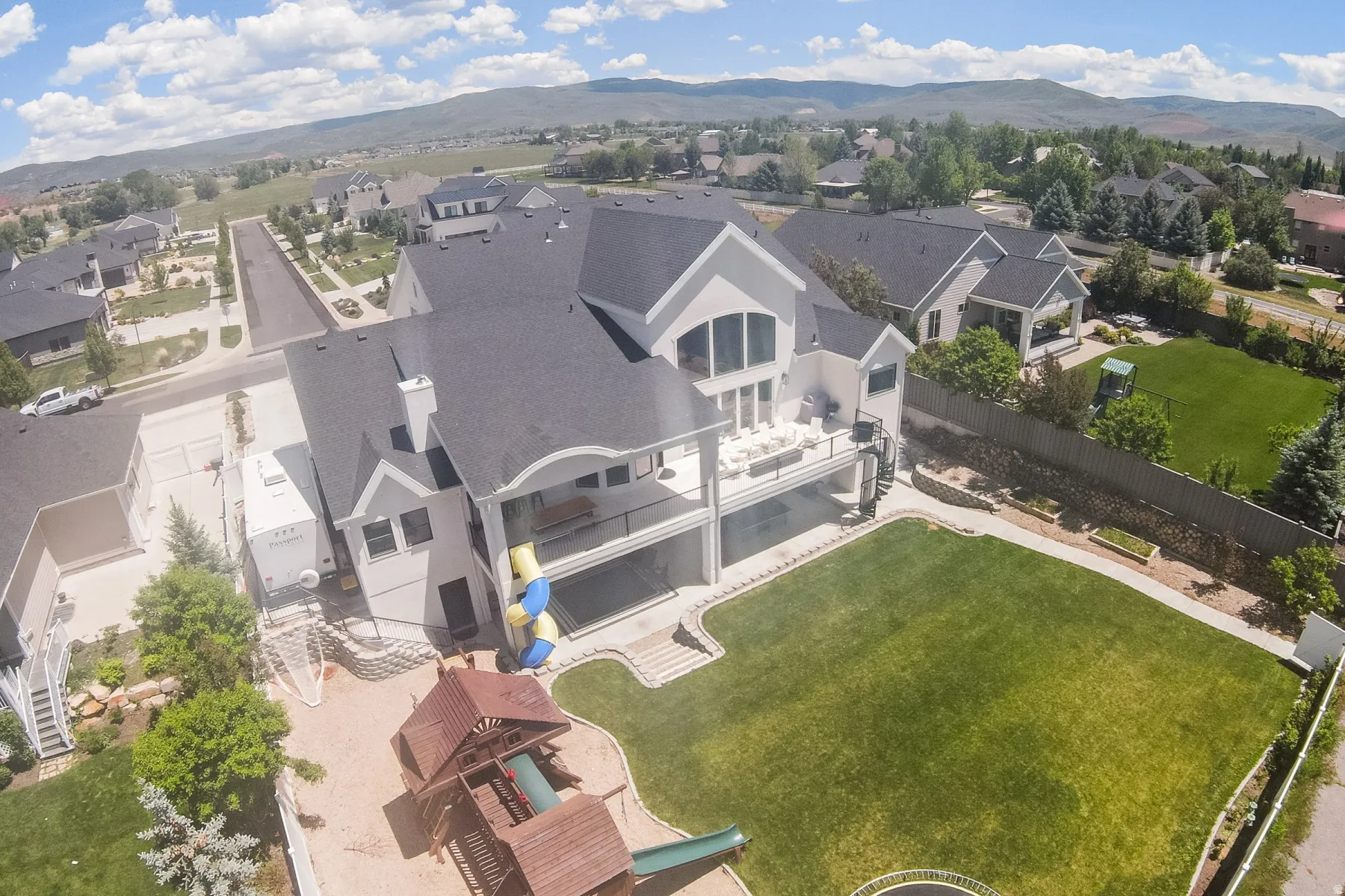 Expansive backyard featuring a large green lawn, multi-level patio, and built-in play structure