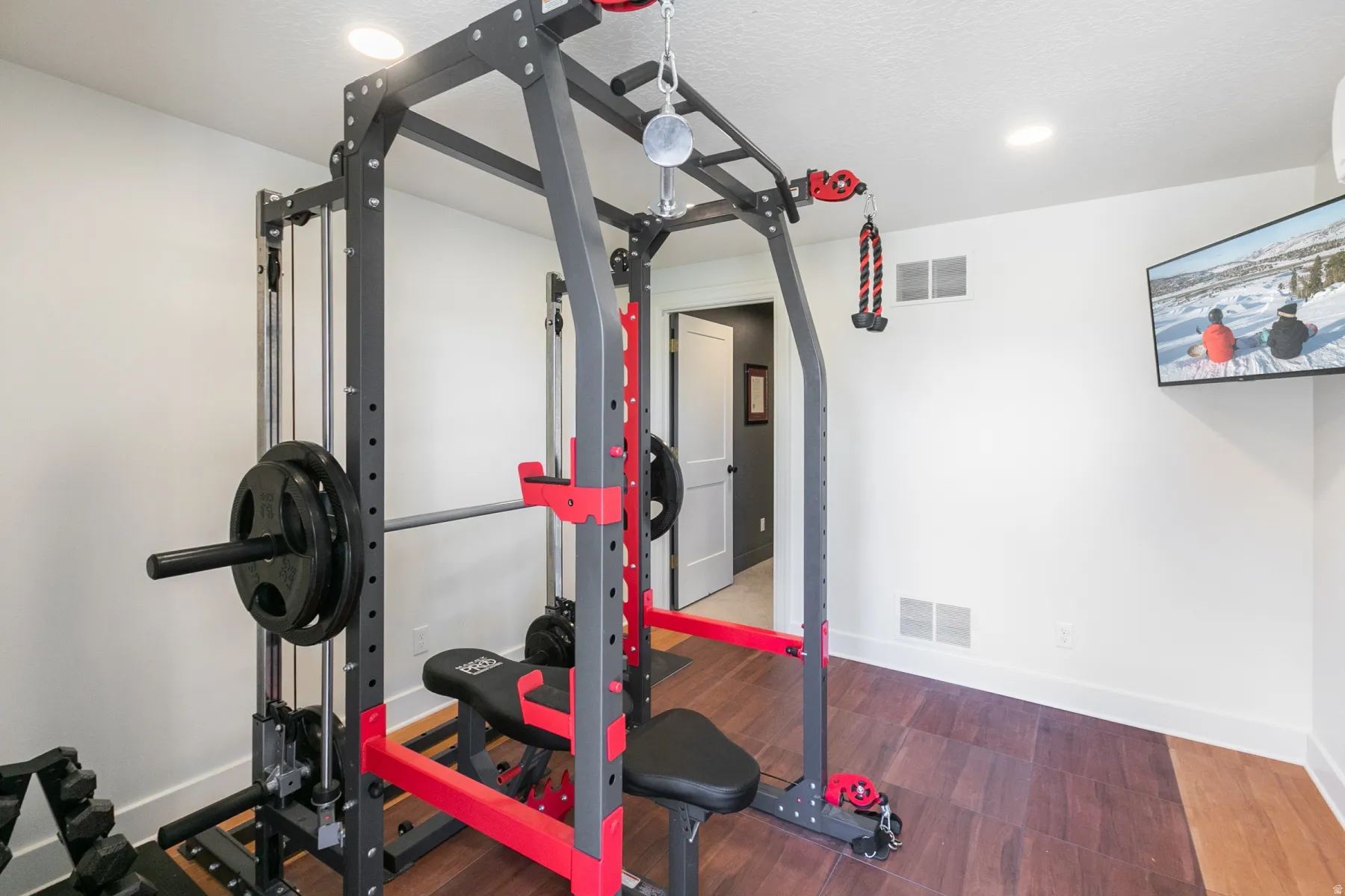 Dedicated exercise space featuring wood-finish flooring, recessed lighting, and a wall-mounted display