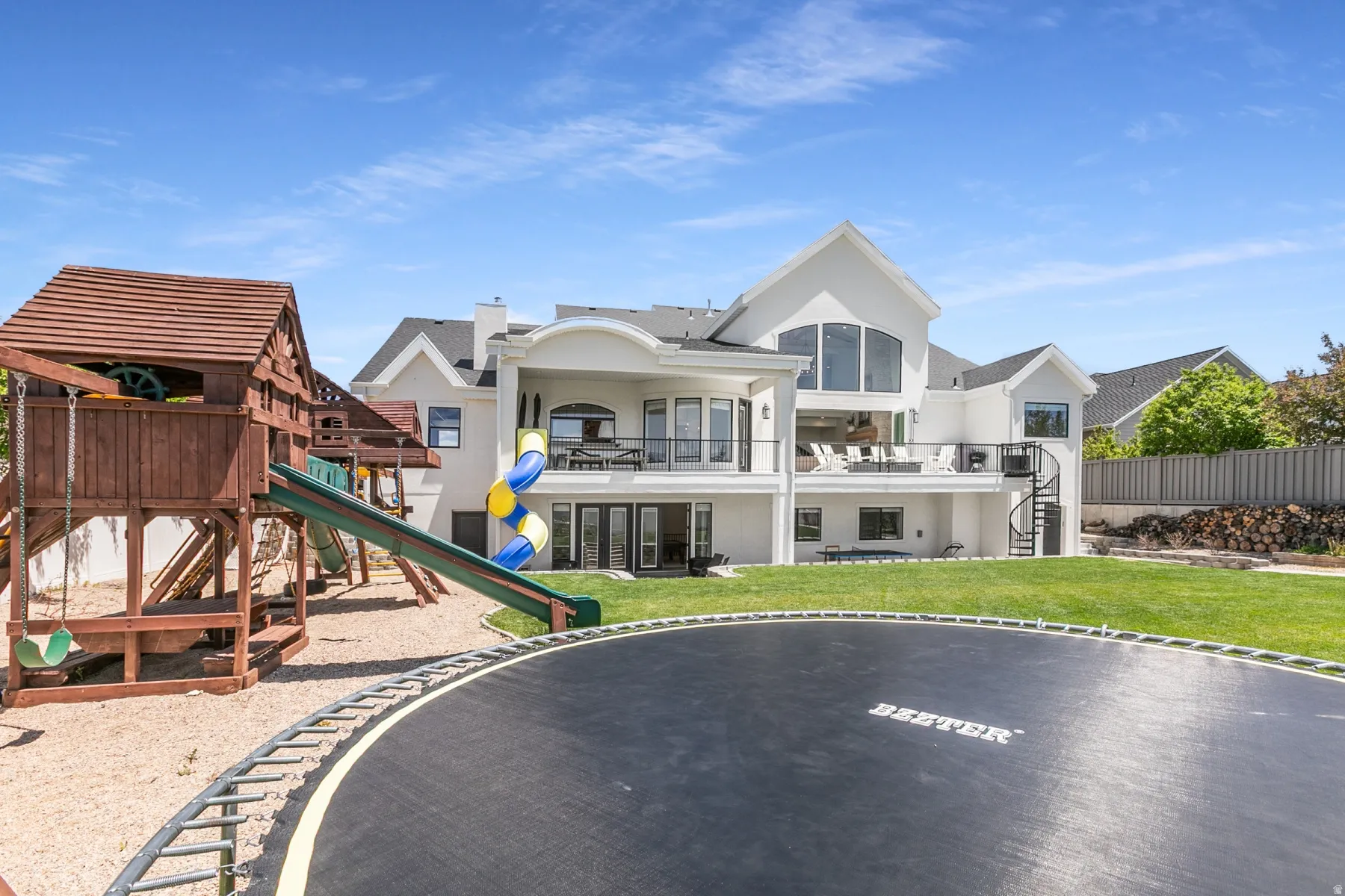 Spacious backyard featuring a manicured lawn, multi-level patio, and a spiral staircase providing exterior access