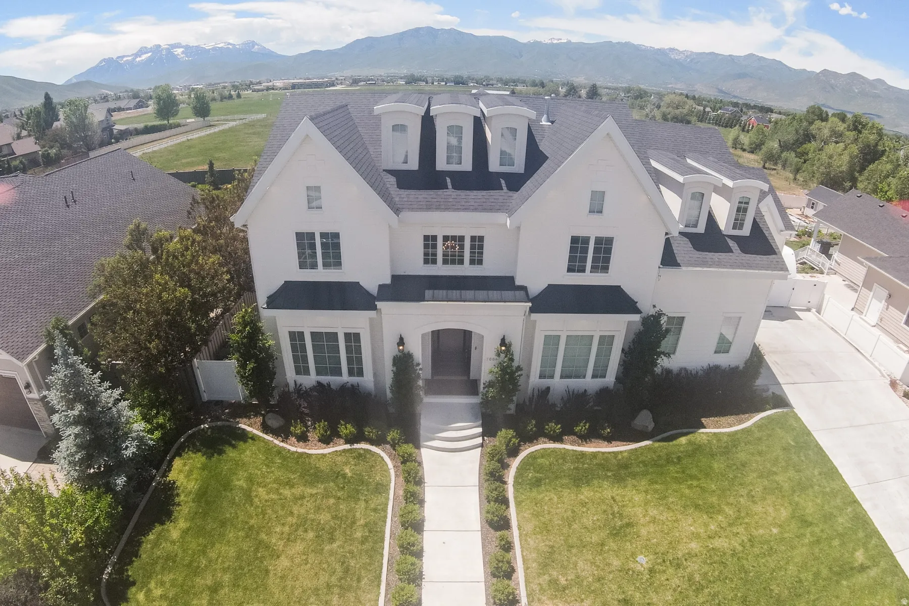 Stately white residence featuring multiple dormer windows, a dark shingle roof, and a prominent front entrance with a complementary arched portico
