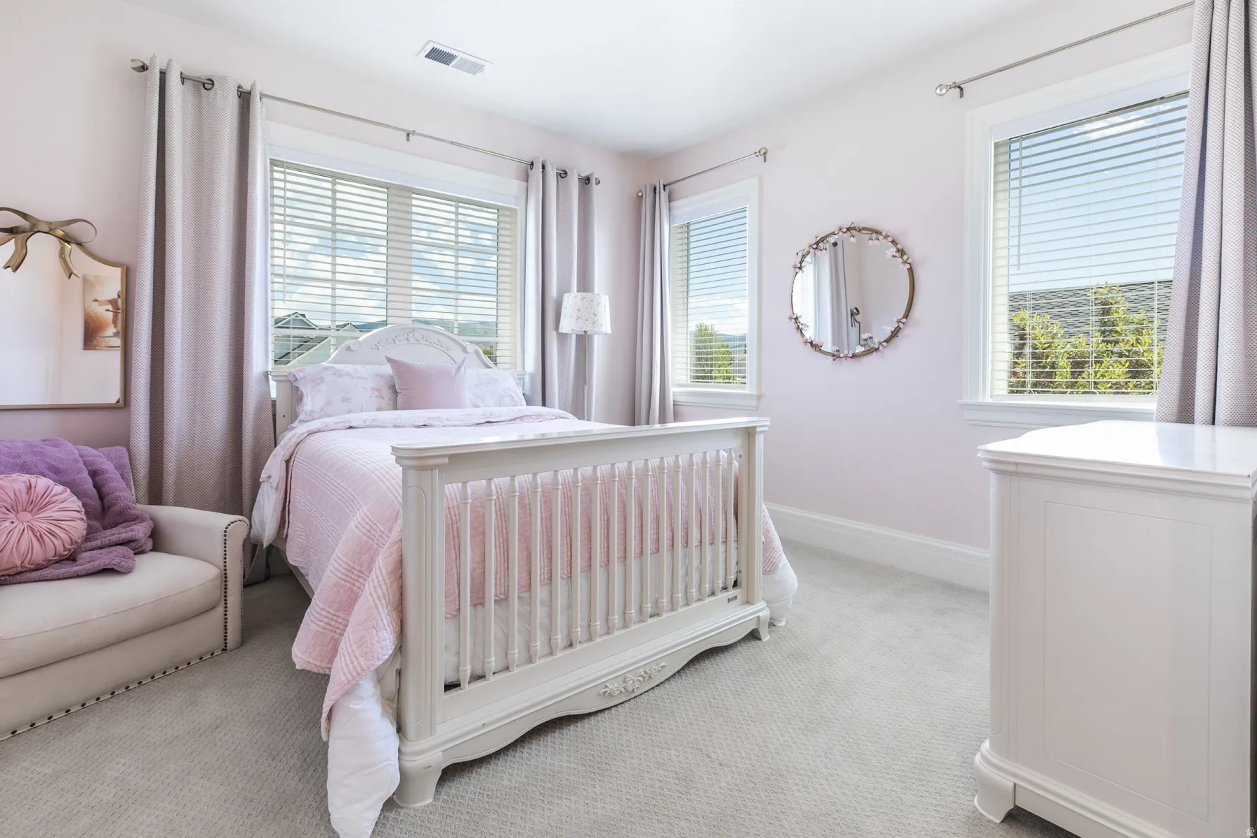 Bright bedroom featuring two large windows with blinds, light wall-to-wall carpeting, and a built-in ventilation system