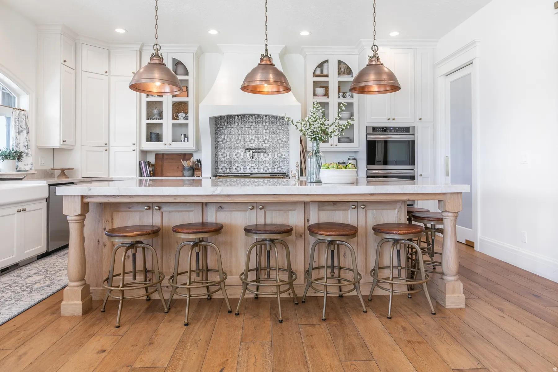 Kitchen featuring a large island with turned wood posts, white cabinetry, integrated stainless steel appliances, and wood-finish flooring