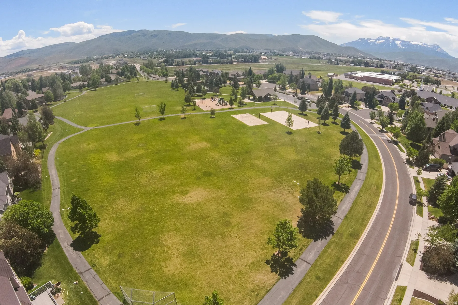 Expansive green space featuring walking paths, mature trees, and recreational courts