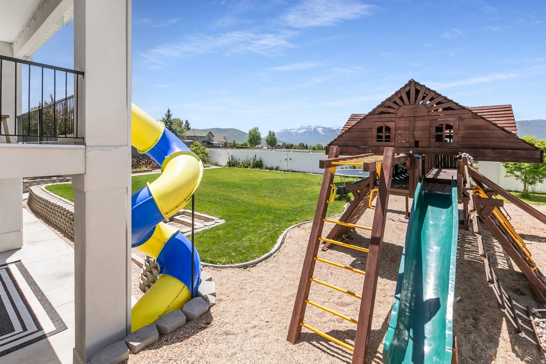 Spacious backyard featuring a large wooden playset with multiple slides and climbing ladders, a spiral tube slide, and a substantial lawn area