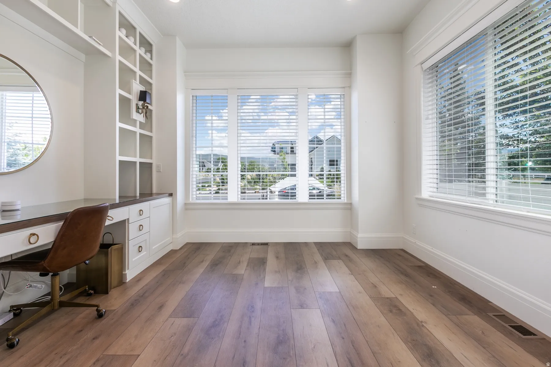 Expansive room featuring wood-finish flooring, white walls, and multiple large windows with blinds