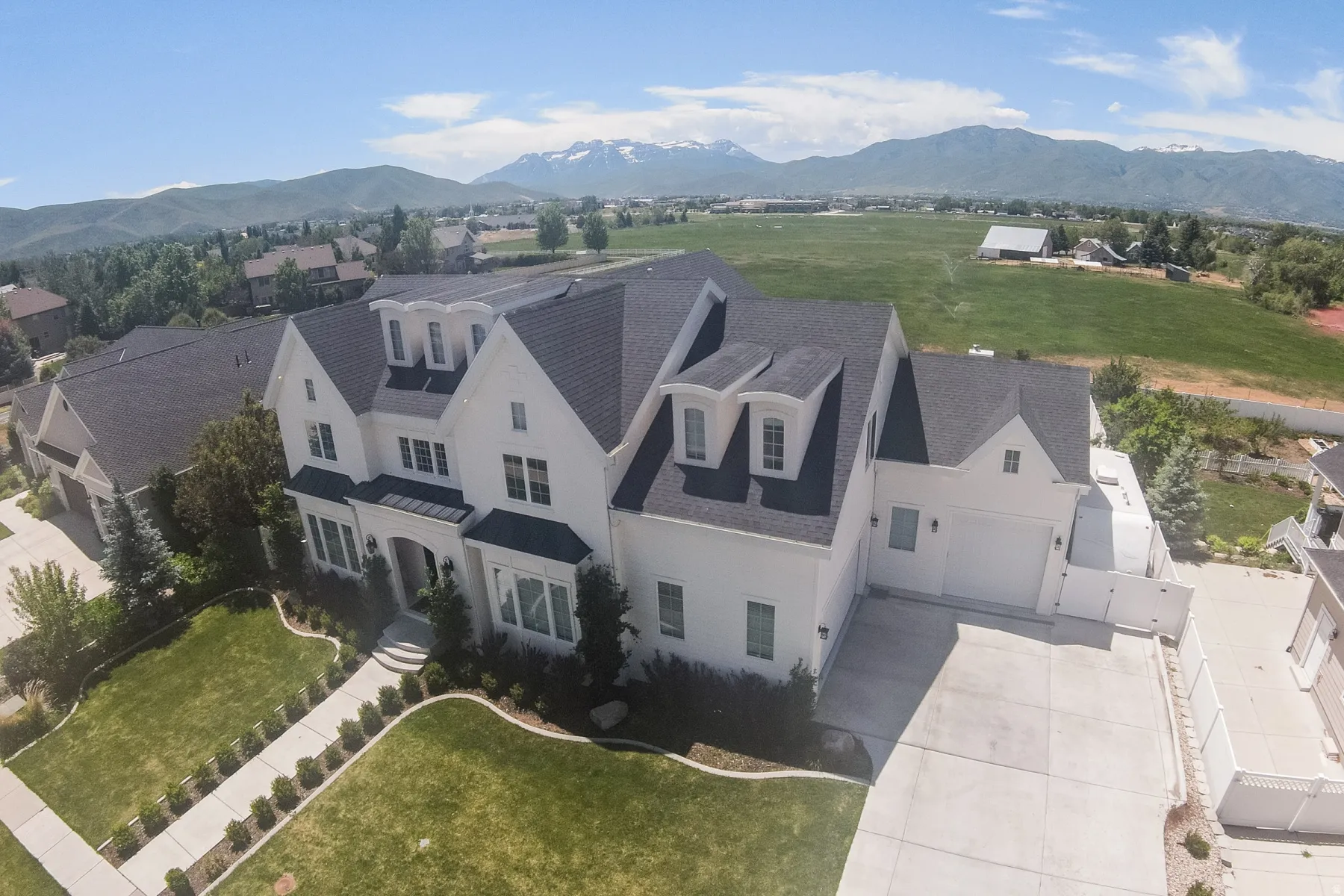 White exterior residence featuring multiple gables and dormer windows, a dark shingle roof, and an arched entry
