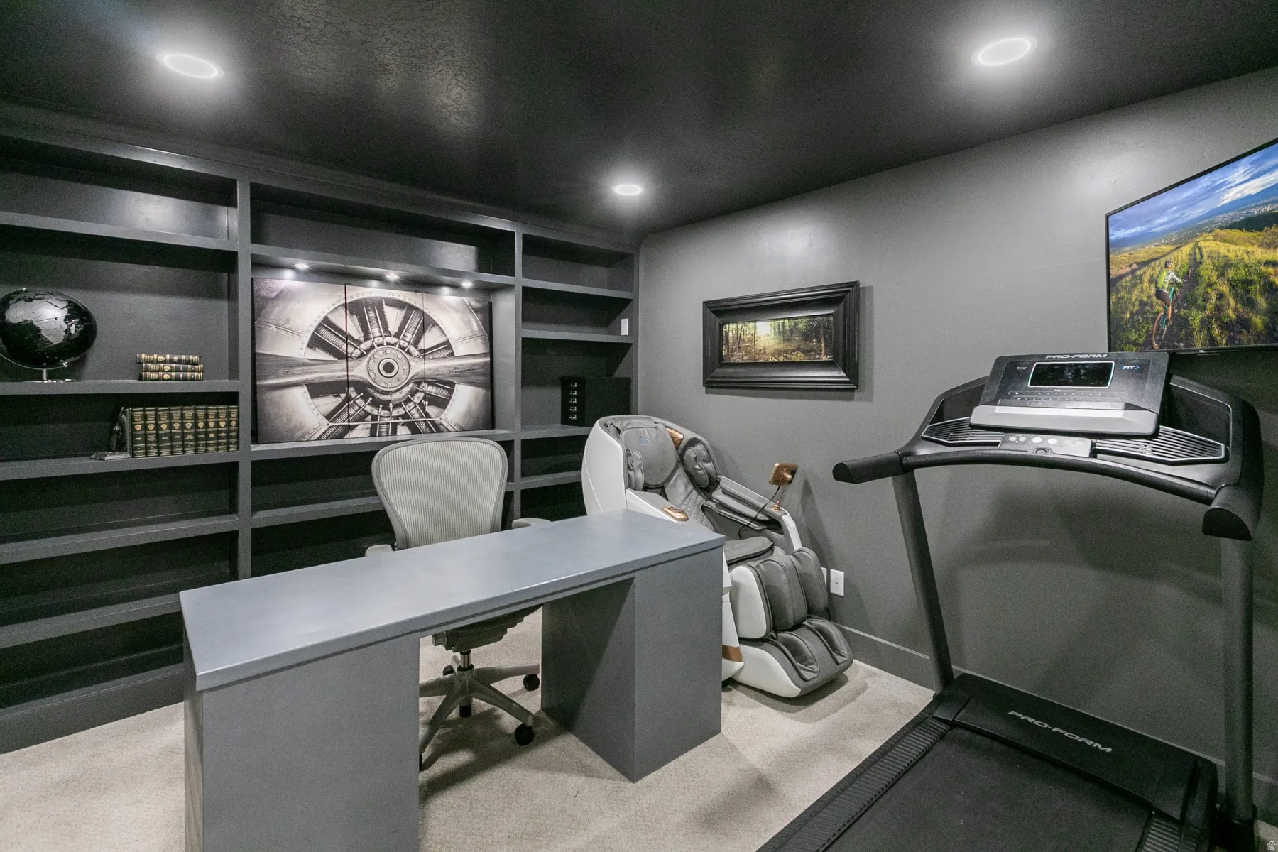 Integrated built-in shelving with accent lighting, recessed ceiling lights, wall-mounted television, and neutral-toned carpeting