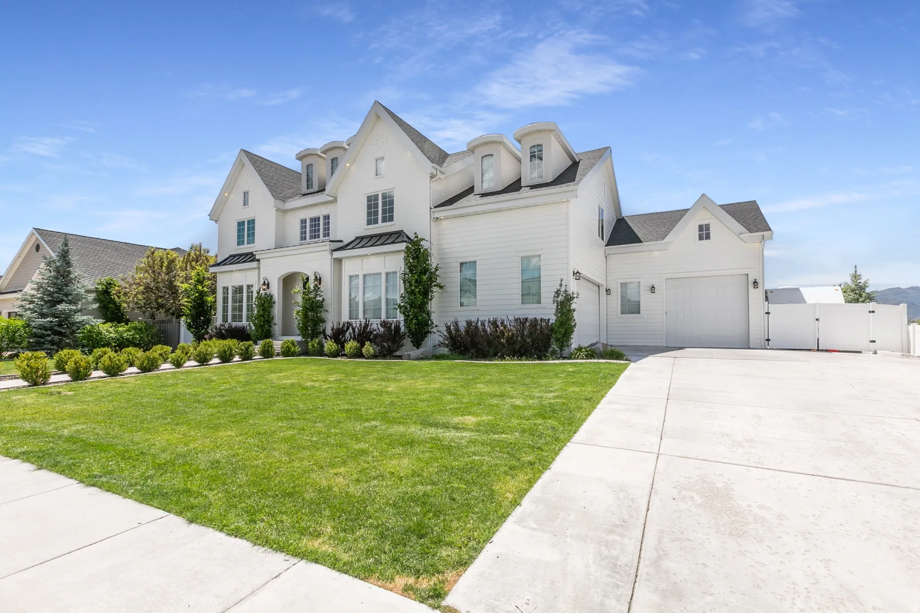 White exterior residence featuring multiple gables, dormer windows, and dark-shingled roofing
