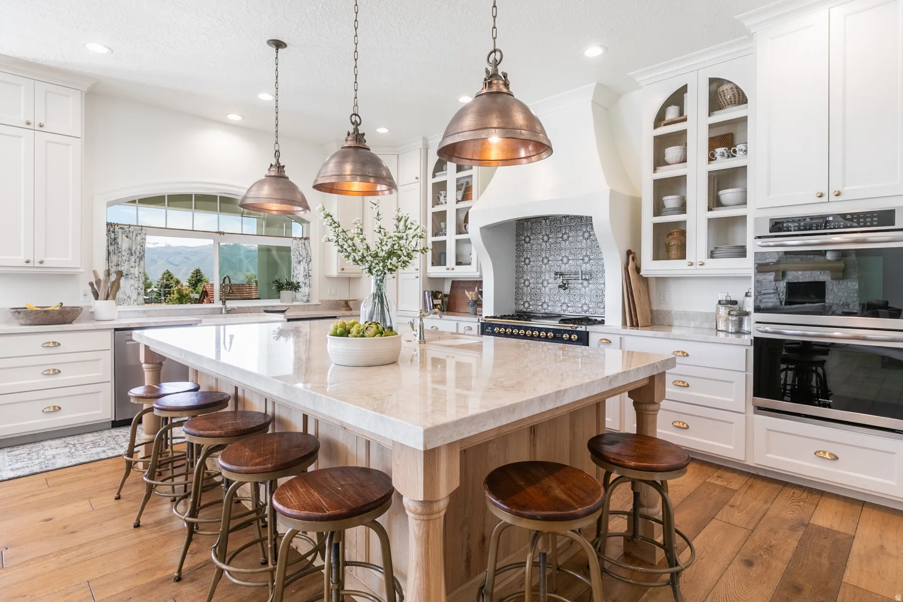 Gourmet kitchen featuring a large central island with seating, integrated double ovens, a gas range with decorative tile backsplash, and extensive white cabinetry