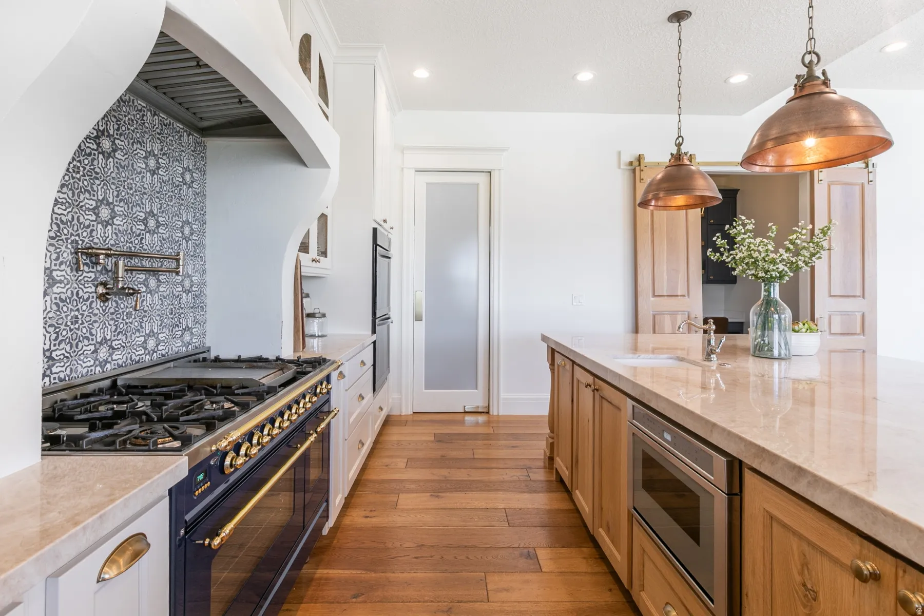 Gourmet kitchen featuring a professional-grade range, patterned tile backsplash, pot filler, light-toned wood flooring, and a large central island with an undermount sink and built-in microwave