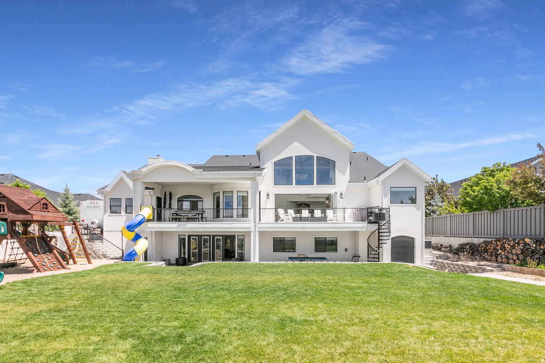 White stucco exterior featuring a large rear lawn, a two-story deck with a spiral staircase, and multiple picture windows