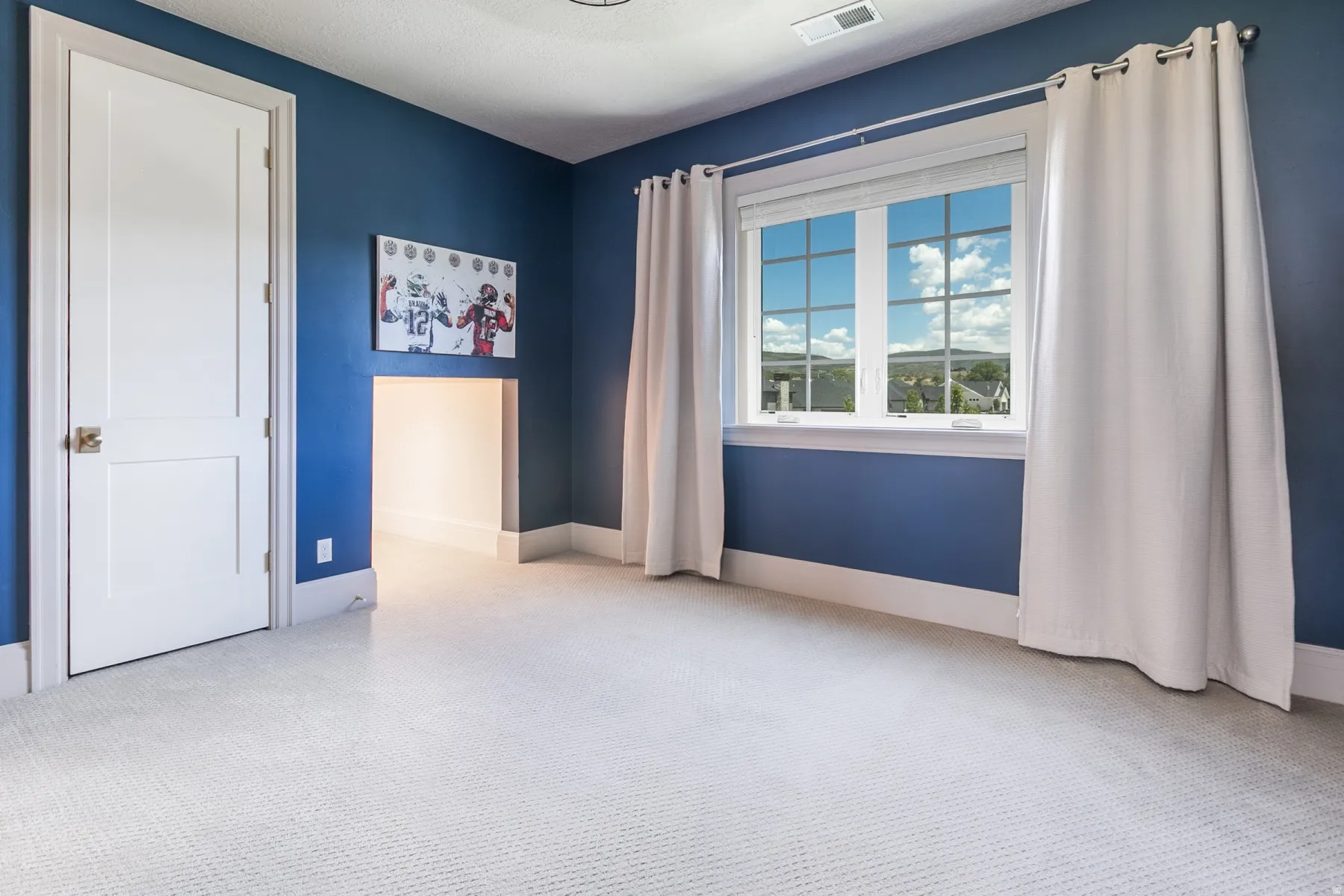 Bright room featuring a large window with grid panes, plush light-toned carpeting, and a built-in recessed niche