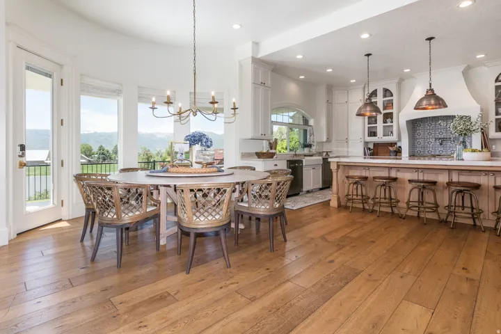 Open-concept dining area and kitchen featuring wood-finish flooring, a curved wall with multiple windows, a decorative chandelier, white cabinetry, and a kitchen island with pendant lighting