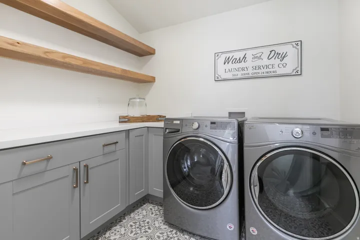 Laundry room featuring two front-loading machines, white countertop, and light gray cabinetry with gold-toned hardware