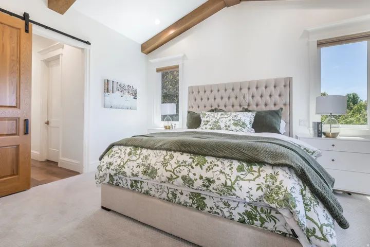 Vaulted ceiling with exposed wood beams, light-toned carpeting, and a sliding barn door entryway