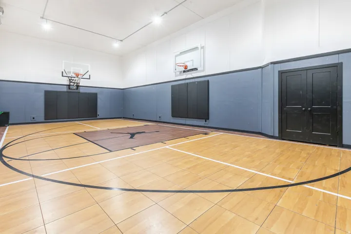 Indoor basketball court featuring light-toned wood-finish flooring, half-court line markings, and two basketball hoops with backboards