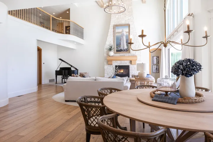 Open-concept living area with wood-finish flooring, a two-story stone fireplace, and a second-story balcony featuring a wood and metal railing