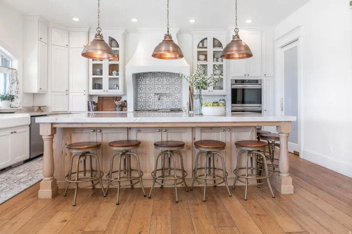 Kitchen featuring a large island with turned wood posts, white cabinetry, integrated stainless steel appliances, and wood-finish flooring