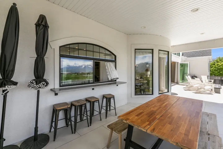 Covered outdoor patio featuring a wood-finish dining table and integrated service window with a stone-finish countertop