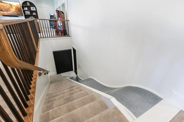 Carpeted staircase featuring a wood-finish handrail and black balusters
