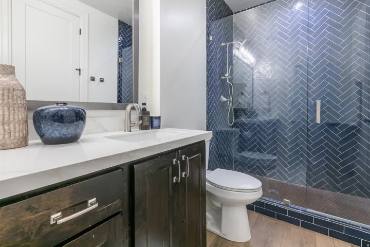 Bathroom featuring a glass-enclosed shower with blue herringbone tile, a dark wood-finish vanity, a white countertop, and a rectangular undermount sink