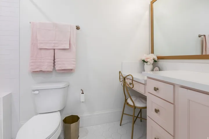 Bathroom featuring a white toilet, hexagonal floor tiles, a light pink vanity with white countertops, a built-in makeup vanity, and a framed mirror